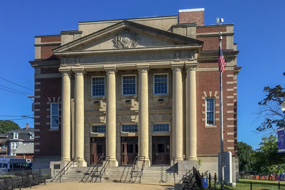 The columned brick Hyde Park Municipal Building in Boston under a bright blue sky