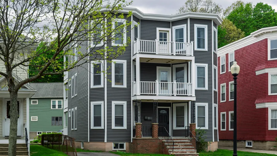 Renovated three-story triple-decker with gray siding, white trim and stacked white porches on a tree-lined street